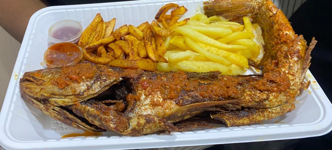 Whole grilled fish served with French fries and fried plantain in a takeaway tray